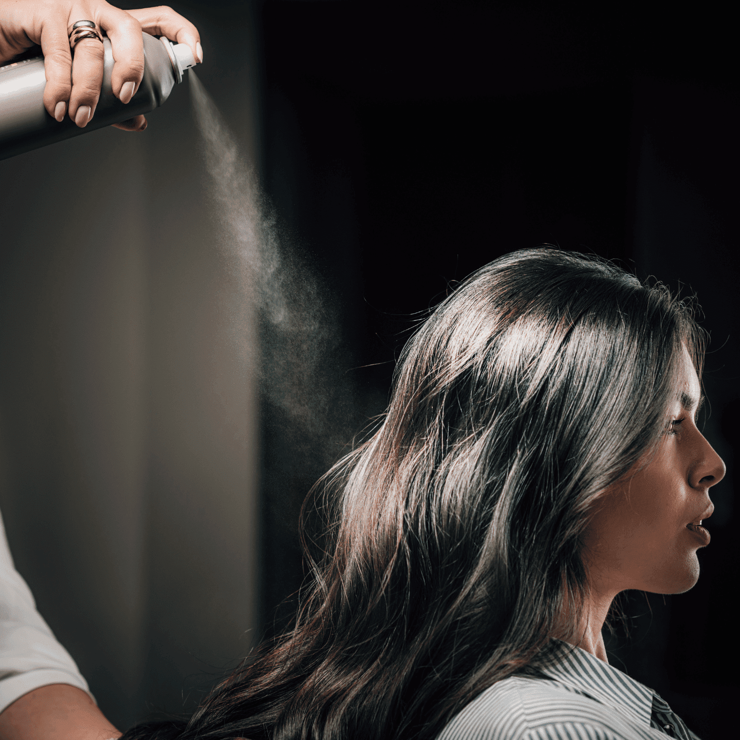 Hair being styled with spray by a hairstylist in a salon setting.