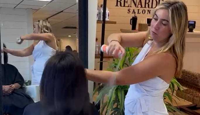 Hair stylist applying spray to client's hair at a salon.