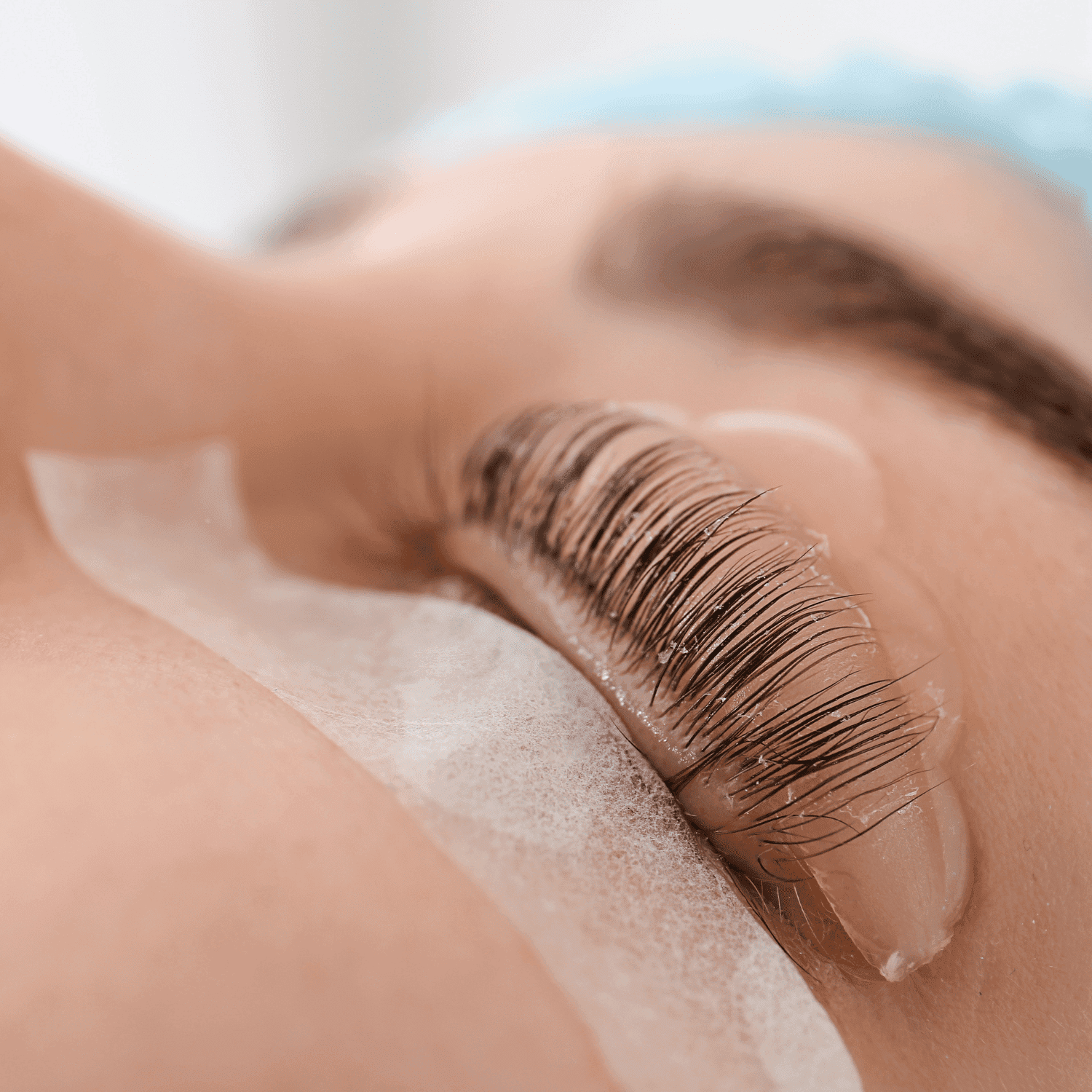 Eyelash treatment in progress with protective pads on a person's closed eye.
