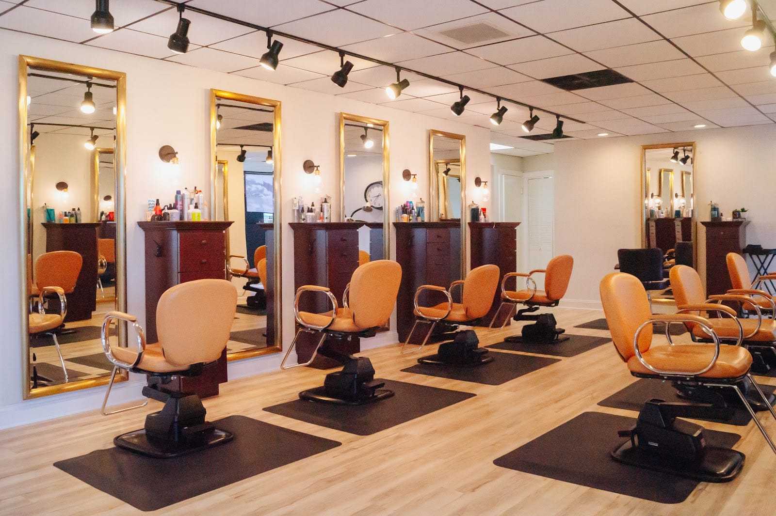 Modern salon interior with mirrored stations and orange chairs.